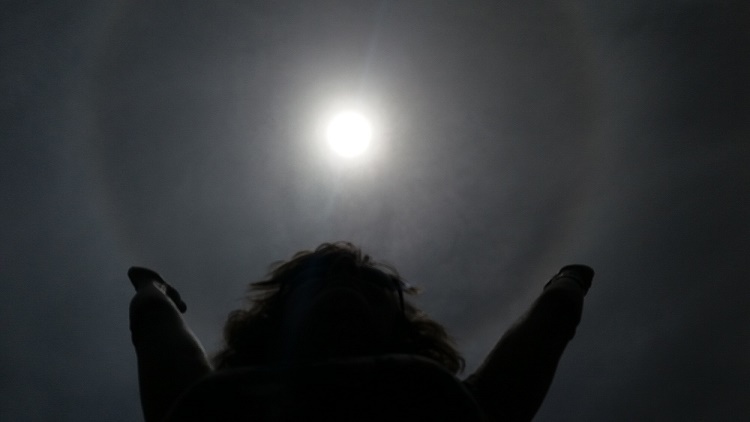 Se ve una persona alzando sus brazos hacia un haro solar.