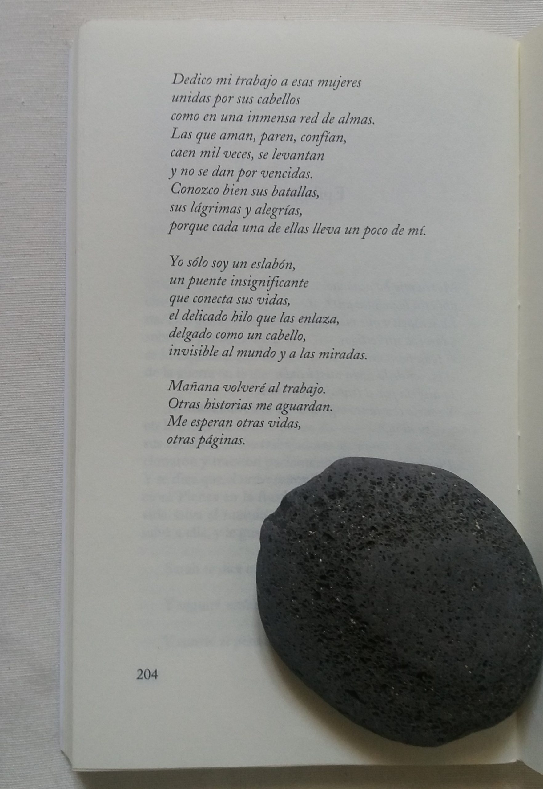 Se ve la hoja de un libro, con un poema escrito. Encima de la hoja, hay una piedra con forma de sombrero. 
