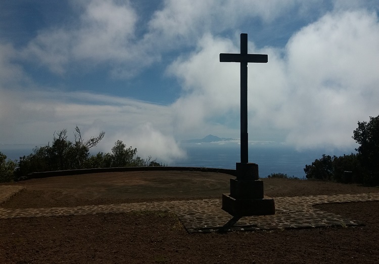 Se ve el Teide en la lejanía, envuelto en nubes. Una cruz en un mirador.