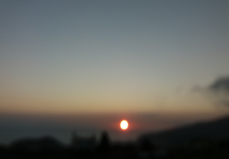 Se ve el sol, un punto desenfocado entre el cielo y el mar.